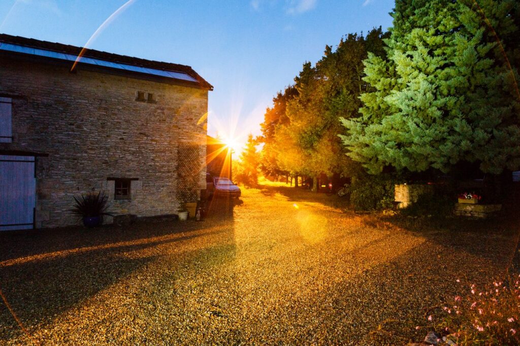 Scenic sunset illuminating a rustic farmhouse in Nouvelle-Aquitaine, France, with vibrant trees and gravel road.